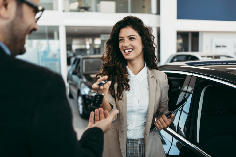 Young professional woman handing car keys to a man in a car dealership