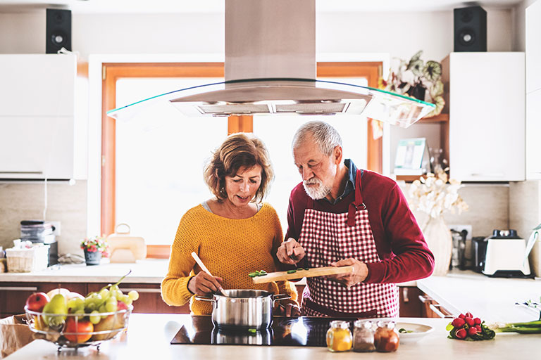 Older couple preparing dinner in a silver pot using a cutting board and array of vegetables