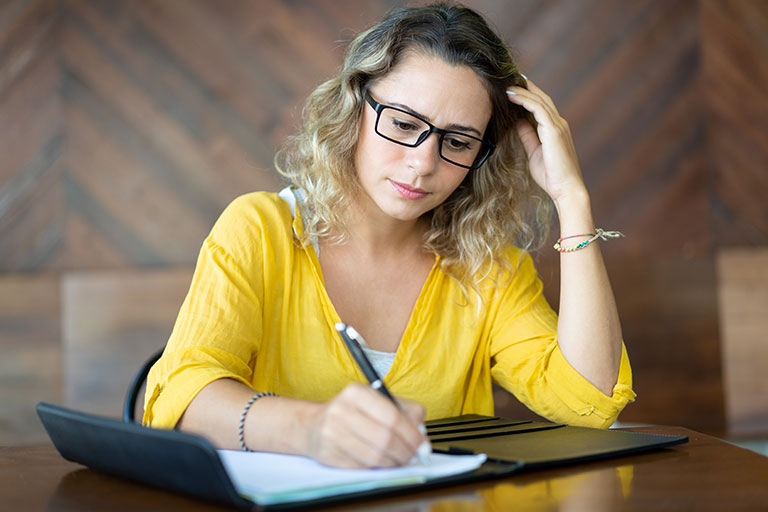 Young blonde woman wearing black rimmed glasses writing in a notepad