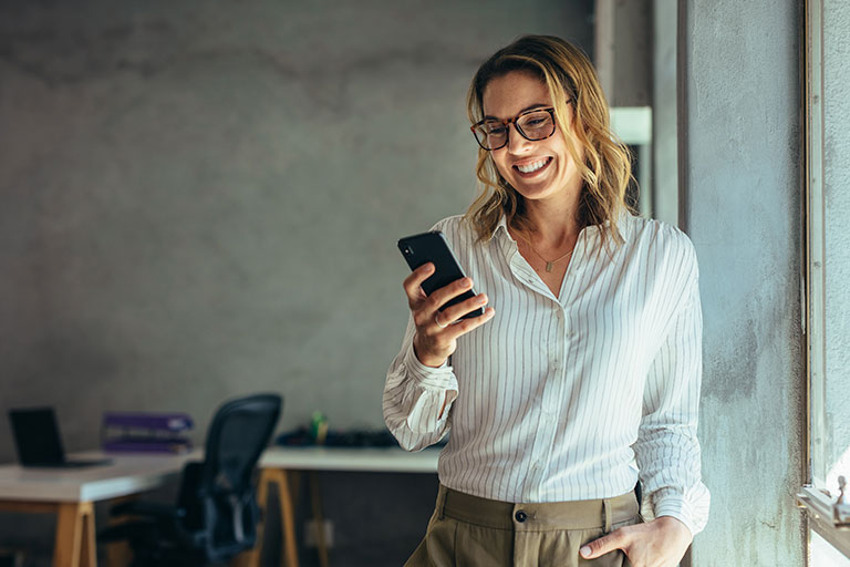 Smiling blonde  businesswoman wearing glassed and business casual attire using cell phone in office