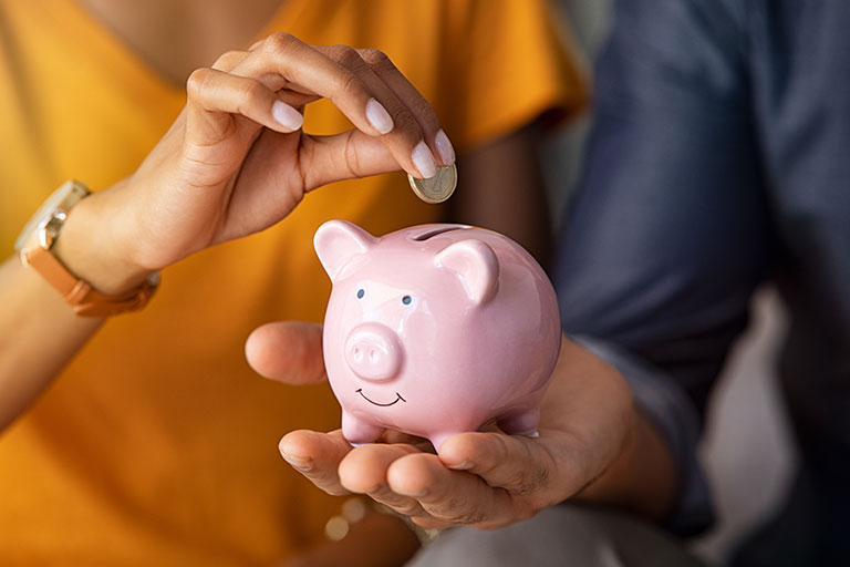 Close up of man holding small piggy bank and woman holding up a coin
