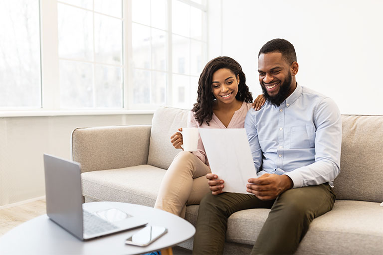 African Amercial couple sitting on couch looking at a piece of paper with laptop and phone on table in front of them