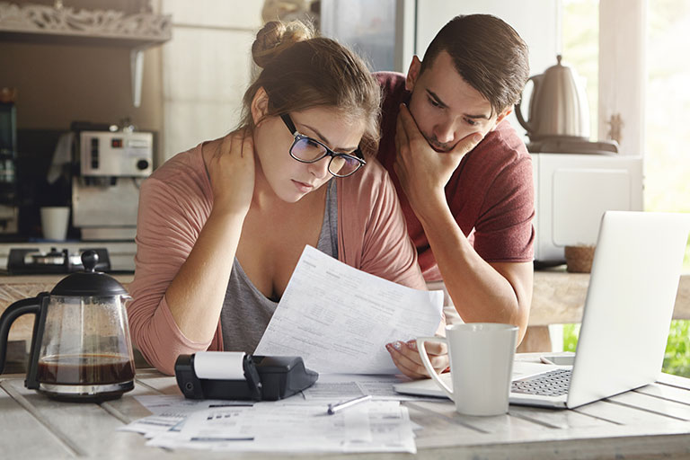 Female in glasses and brunette man studying paper while managing domestic budget together in kitchen